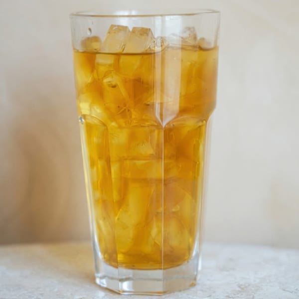 A tall glass filled with iced tea and ice cubes on a light-colored surface.