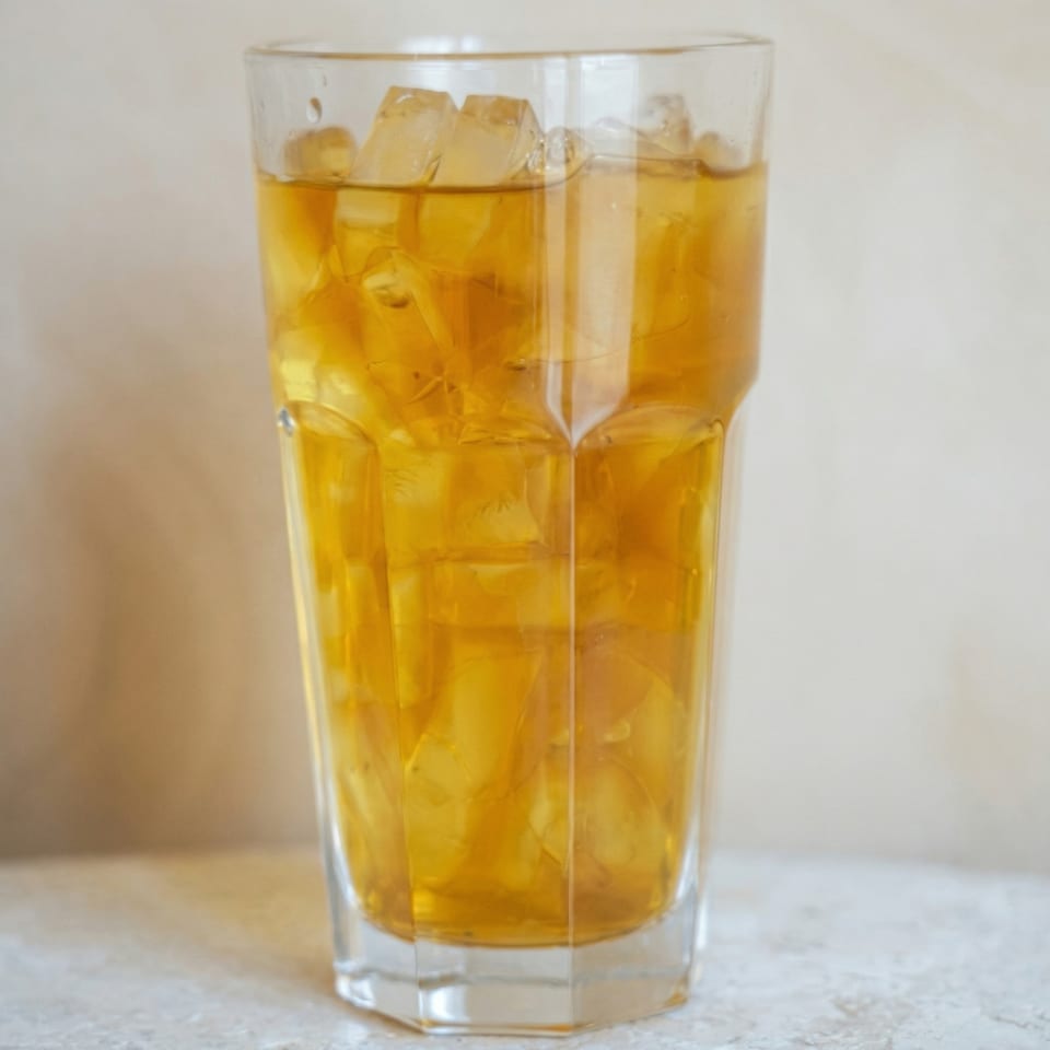 A tall glass filled with iced tea and ice cubes on a light-colored surface.